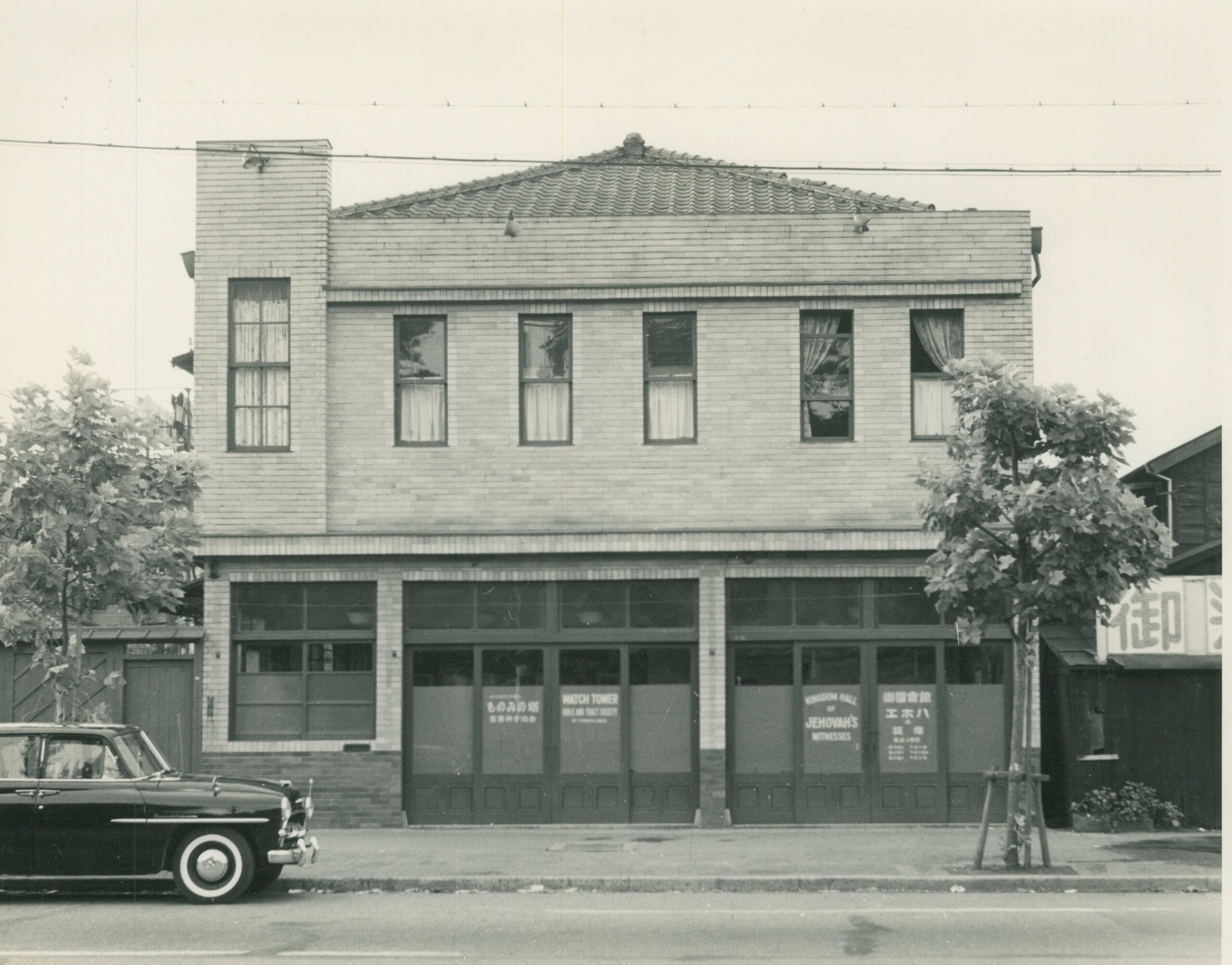 an old photo of a building with a car sitting out front