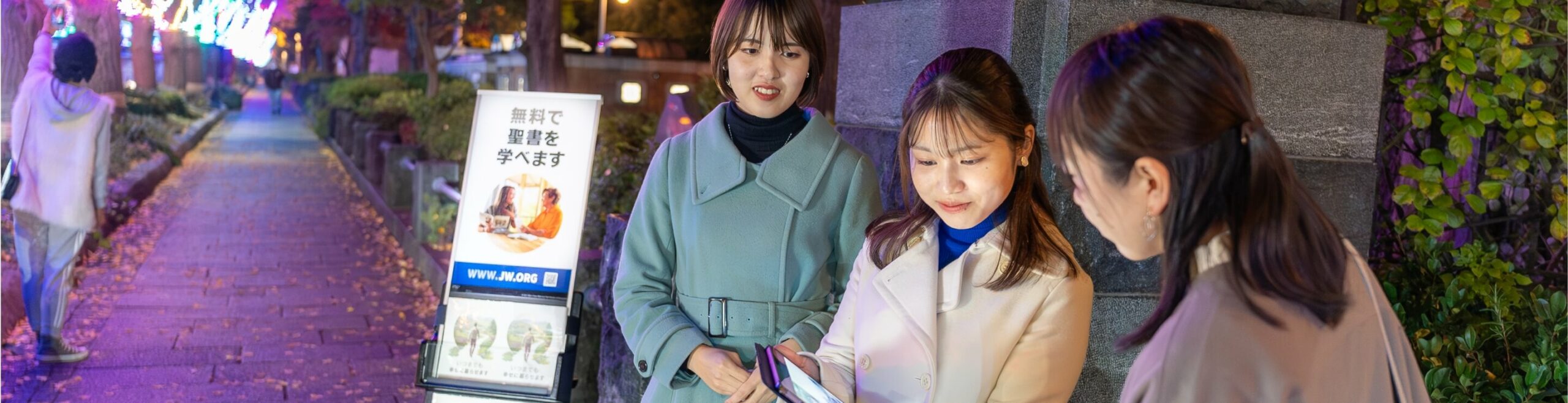 two women standing in front of a public witnessing cart showing a woman something on an electronic device